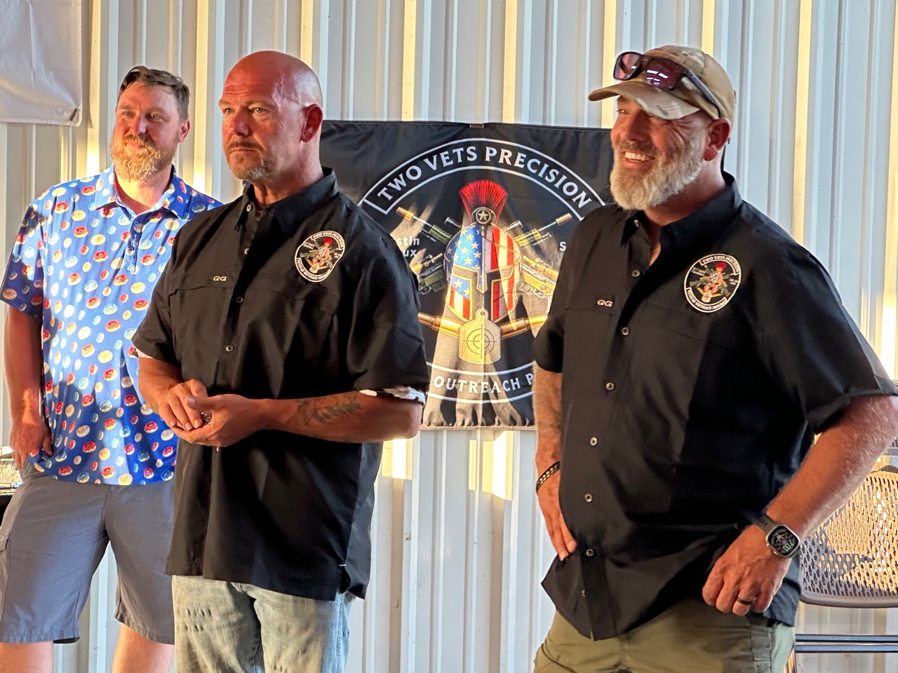 Two Vets Precision representatives standing together in front of the outreach program banner