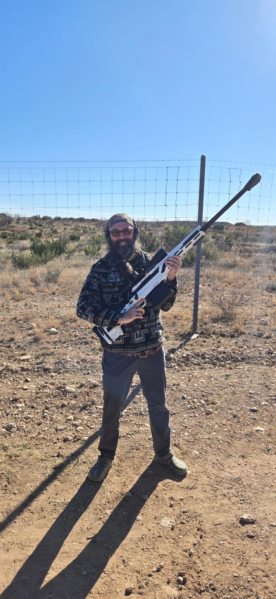 A veteran holding a white precision rifle in the West Texas landscape