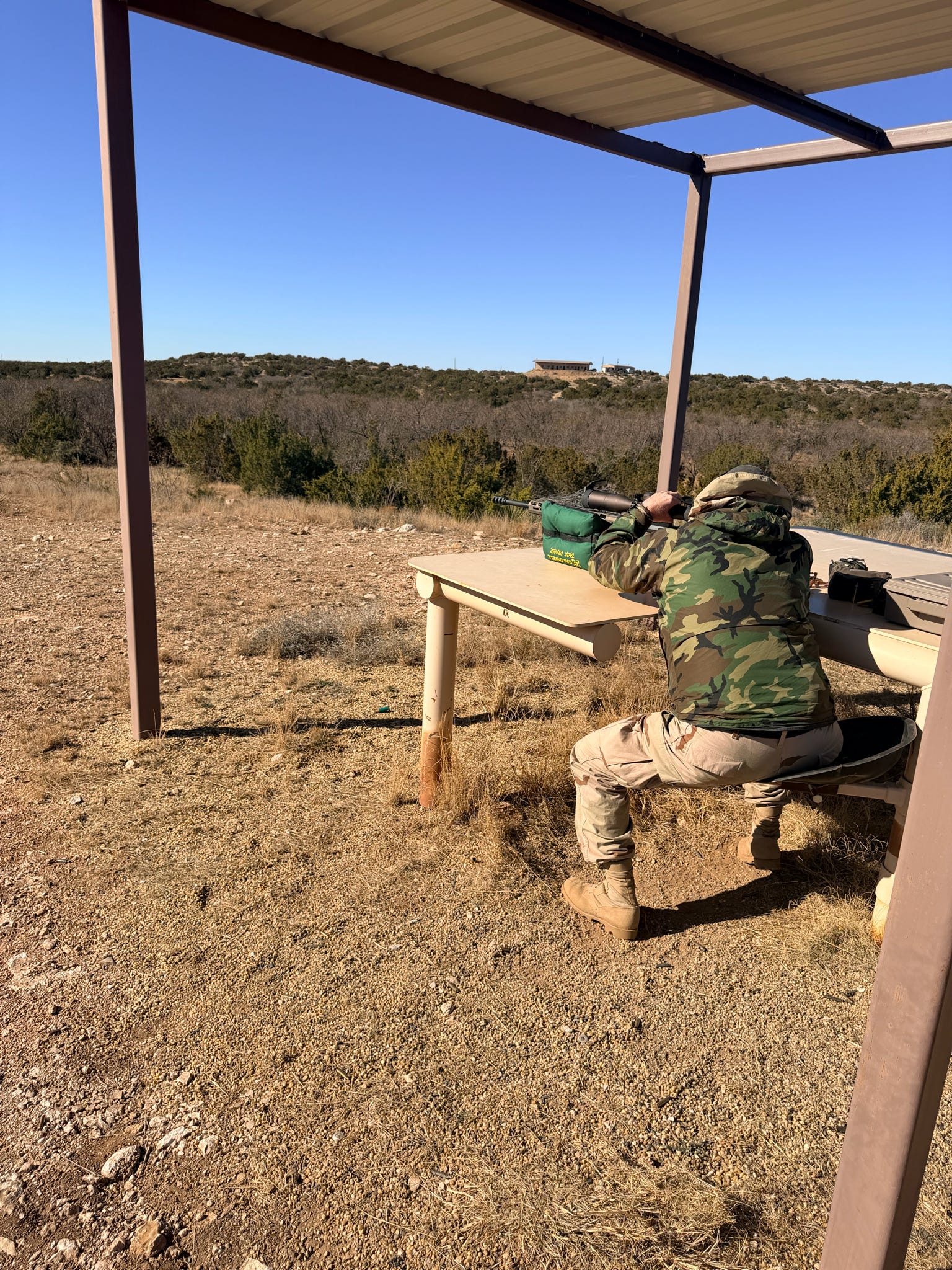 A camouflaged shooter taking position under the range shelter