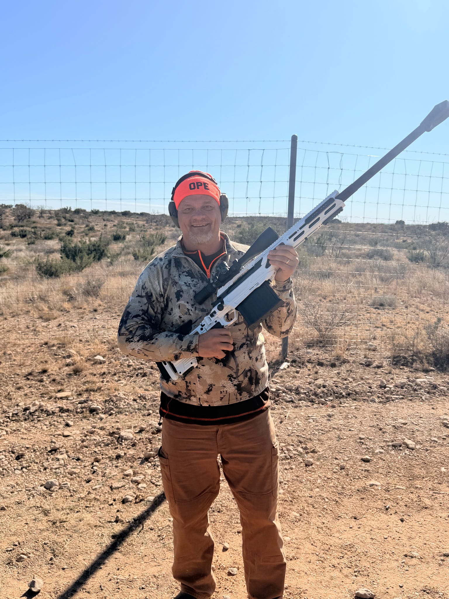 A smiling veteran holding a white precision rifle after time on the range